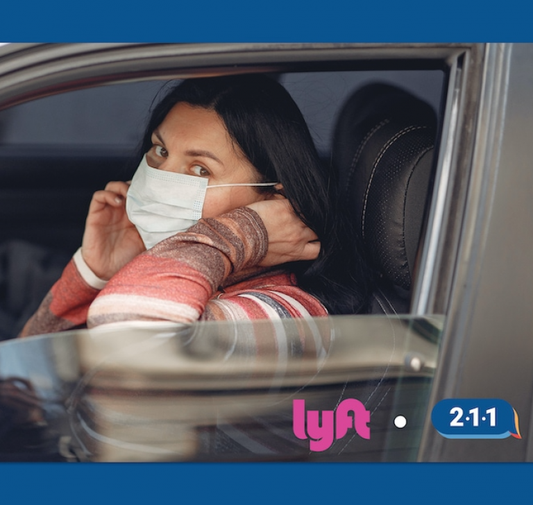 A woman wearing a mask riding in a car. Logos for Lyft and 211 are on this image.